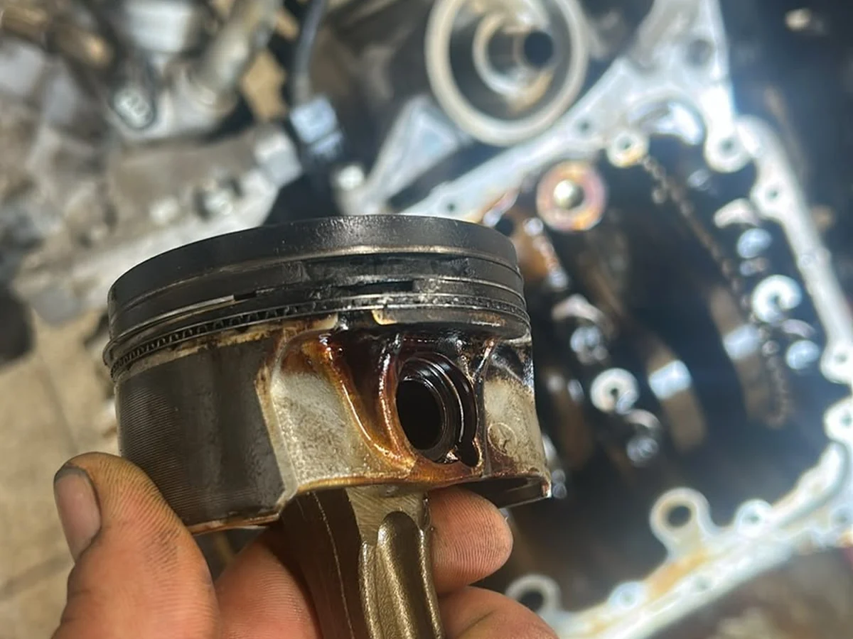Mechanik drží poškozený píst vyjmutý z motoru